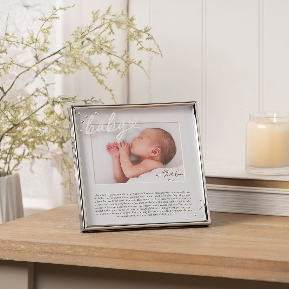 Silver metal photo frame with "baby" script and heart detail, holding a 6 x 4in landscape photo with printed verse below, shown on a wooden table with candle and foliage.