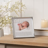 Silver metal photo frame with "baby" script and heart detail, holding a 6 x 4in landscape photo with printed verse below, shown on a wooden table with candle and foliage.