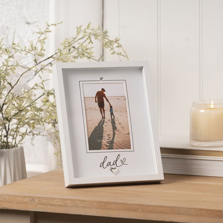 White wooden easel photo frame with 'dad' script and small silver heart, displaying a beach photo of father and child, shown on a wooden table.