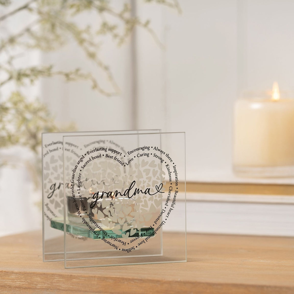 Square clear glass tealight candle holder printed with "grandma" in black script and a circular ring of heartfelt words, shown on a wooden surface beside a lit candle.