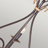 A close-up of an ornate arm from the Windermere 3 Light Chandelier in Rust/Gold, showcasing gold accents and a decorative exposed bulb. The soft gray background emphasizes the chandelier's elegant details and traditional design.