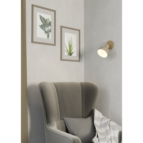 Wonvora wall spotlight in a corner above an armchair, single dome shade in sandy steel on a wood-grain plate with a satin nickel swivel pin, lit beside framed botanical prints.