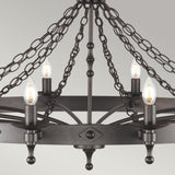 The Warwick 12 Light Chandelier - Graphite Black showcases a graphite black finish with twelve candle-like bulbs, suspended from decorative chains. Its circular and geometric design reflects medieval craftsmanship, offering a classic elegance against the light gray background.