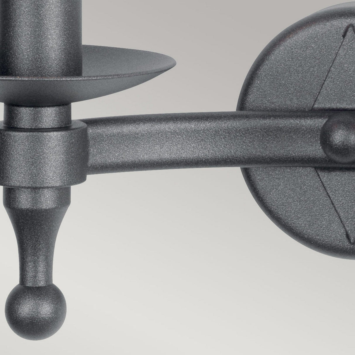 Close-up of a metal wall-mounted arm bracket in graphite black with a round base, featuring a hand-forged design and a curved structure that exudes medieval charm, complete with a spherical end. This intricate piece beautifully contrasts against the soft, light gray background of the Warwick 2 Light Wall Light.