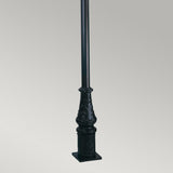 The Wilmslow 1 Light Lamp Post in black features an ornate, decorative base and stands against a plain gray background. Made from durable cast aluminum, this lamp post showcases intricate designs and a sturdy square base, offering a classic or Victorian-inspired style perfect for outdoor lighting scenarios.