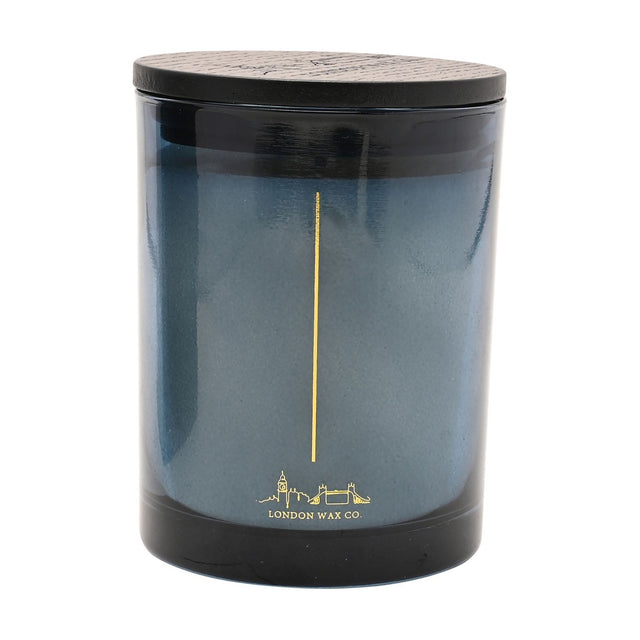 Dream & Cocoon round scented candle in a blue glass vessel with black lid, gold wick line and London skyline design, on a plain white background.