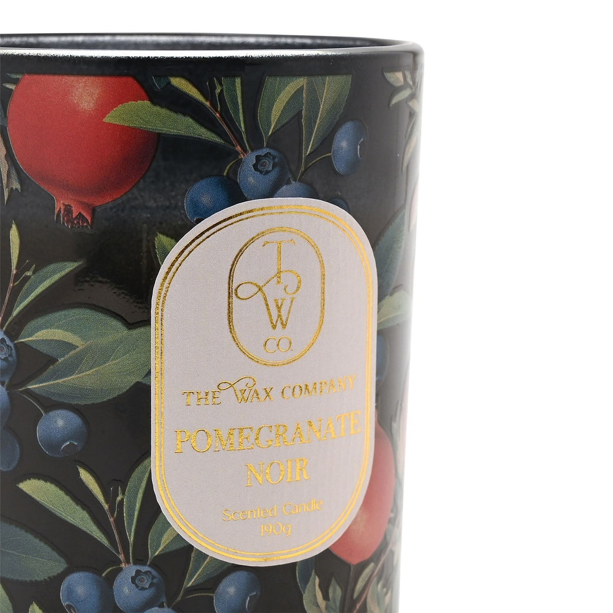 Close-up of Pomegranate Noir scented candle in black glass jar with pomegranate, blueberry and leaf print, gold-edged label reading "Pomegranate Noir", 190g.