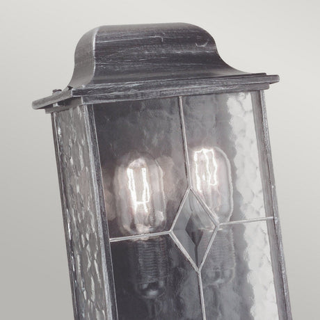 A detailed view of the Wexford 2 Light Outdoor Wall Light - Black/Silver, highlighting its vintage design with hand-leaded glass panes and an elegant diamond-shaped embellishment. This outdoor wall lantern showcases two Edison bulbs, softly illuminating a neutral backdrop and embodying traditional sophistication.