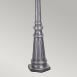 The Wexford 2 Light Lamp Post - Black/Silver showcases a robust black metal base with vertical grooves, ideal for outdoor lighting. Its sleek design contrasts beautifully against a light gray background, offering an elegant touch to any setting.