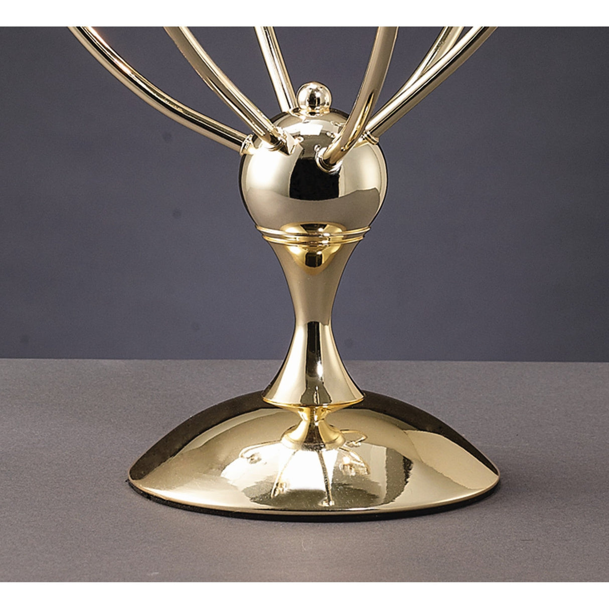 A close-up of the Xeena 3 Light Crystal Table Lamp’s shiny French gold base and lower structure, reminiscent of a modern lamp or award, set against a plain gray background.