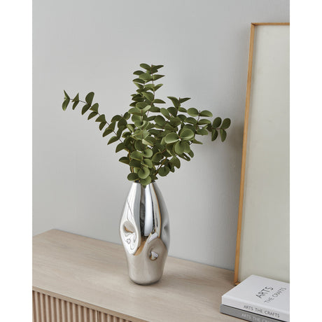 Xiporai Glass Vase 28.5cm in mirror chrome with dimpled ovoid body, holding eucalyptus stems on a wooden sideboard against a light grey wall.