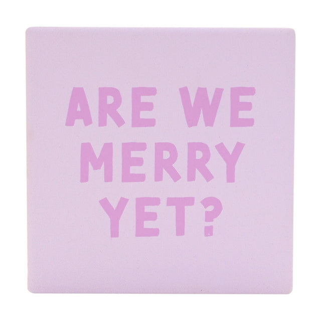 Square ceramic Christmas coaster in soft purple with "Are We Merry Yet?" printed in chunky orchid pink capitals, matt finish, shown on a plain white background.