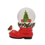 Red resin Santa boot snow globe with a robin on the toe, holly and berry cuff, and a Christmas tree with gifts inside the dome, on a white background.