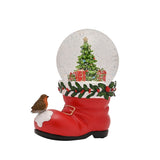 Red resin Santa boot snow globe with a robin on the snowy toe, holly-trimmed cuff, and a decorated Christmas tree with gifts inside the dome, on a plain white background.