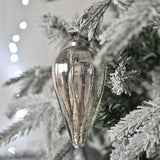 Large teardrop Christmas tree decoration in heavy ribbed glass with an antiqued silver finish, hanging from a snow-dusted tree branch.