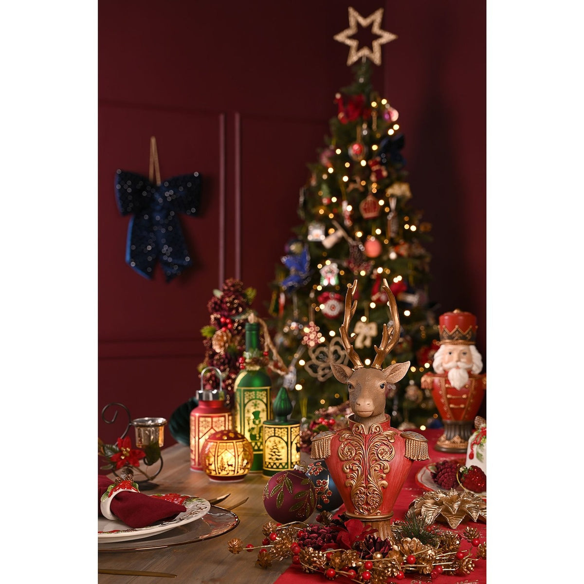 Reindeer Bust Figurine 30cm with gold antlers, red military-style jacket and gold scrollwork, displayed on a Christmas table setting near a decorated tree.