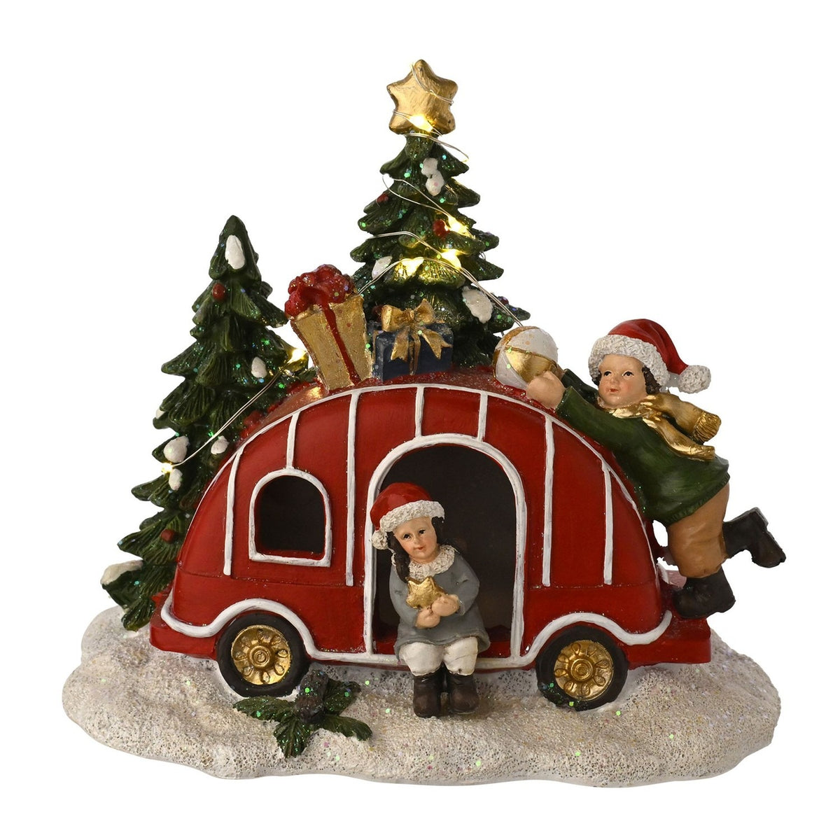 Light-up red Christmas Caravan decoration with gift boxes and gold star on roof, two children in Santa hats beside snow-dusted trees, on white background.