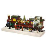 Light-up Christmas train with red engine, gold chimney, wagon of presents, teddy bear and mini tree on a snowy base with Santa and children figures.