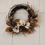 Faux Magnolia Iron Semi Wreath, 40cm, with cream magnolia blooms, pinecones, bronze leaves and bare twig branches, hung on a light neutral panelled wall.