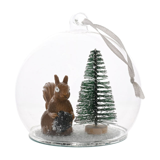 Clear round glass bauble Christmas decoration with a brown squirrel holding a pine cone beside a green bottle-brush tree on a snow-flecked base, hung by a grey ribbon on a white background.