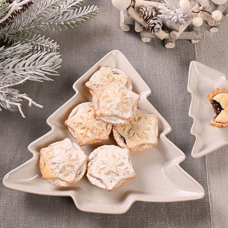 Christmas Tree Speckled Stoneware Plate 26cm in off white holding snowflake-topped iced mince pies, set on a grey textured tablecloth with festive decor.