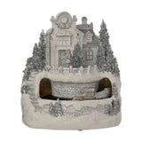 White resin Christmas village LED decoration with a clocktower building, smaller house, silver glitter pine trees, and a moving train through a tunnelled hillside base.