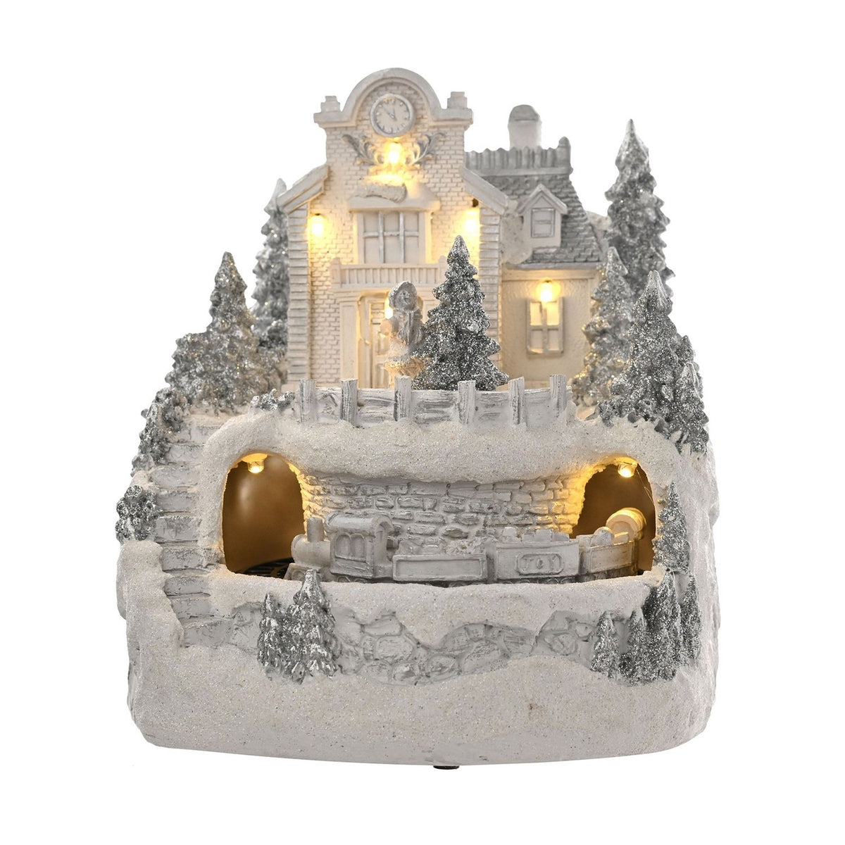 White resin Christmas village LED decoration with clock-tower building, dormer-window house, glitter pine trees, fenced terrace, and a train through stone tunnels, on white background.