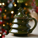 Green stoneware Christmas tree mug with polka dot design, tiered body, curved handle, and star-topped lid, shown against festive bokeh lights.