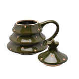 Green stoneware Christmas tree mug with peach polka dots in three rounded tiers, curved handle, and star-topped lid shown removed beside it on a white background.