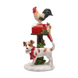 White resin Christmas ornament of a cockerel atop a snow-capped red mailbox with parcels, beside a spotted dog holding a Santa letter, with holly accents on a snowy base.