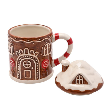 Ceramic gingerbread house mug in glossy brown with raised white icing detail, candy-cane striped handle, and a separate snowy roof-shaped lid, shown on a white background.