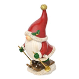 Skiing Santa Gonk resin tabletop Christmas decoration in red, featuring a tall pointed hat with gold pompom, white fur trim, holly sprig, and ski poles, shown on a plain white background.