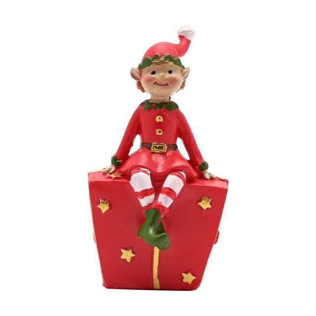 Jingle Elf resin figurine in a red suit with green collar and cuffs, striped stockings, seated on a red gift box with gold stars, on a white background.