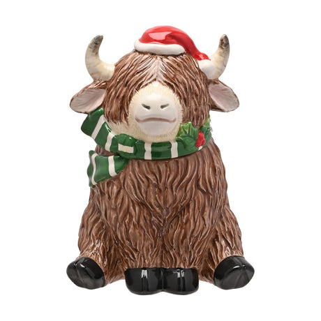 Christmas Highland Cow Ceramic Biscuit Barrel, 24.5cm, brown shaggy coat with cream horns, red Santa hat and green striped scarf, seated pose on plain white background.