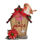 Robin bird house resin figurine with light-up window, a robin perched on a snowy red roof with holly and a bow, "peace" in red script, poinsettia and snowflake detail, on a white background.