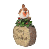 Merry Christmas Robin Sitting on a Log Figurine in brown, with holly and berries at its base and "Merry Christmas" carved into the wood grain, shown on a plain white background.