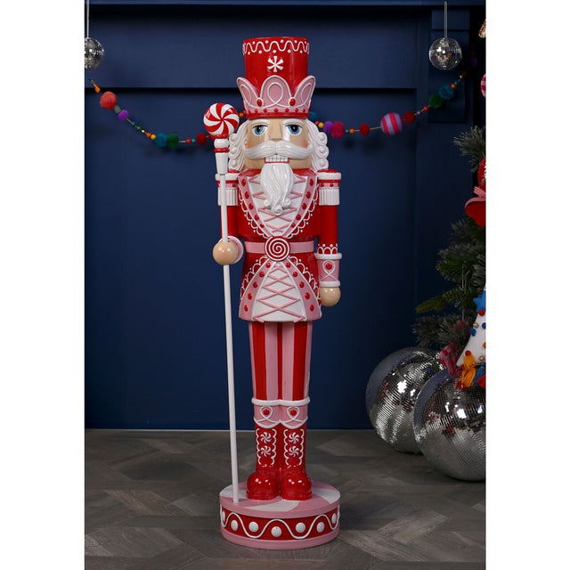 Giant 92cm resin Christmas nutcracker ornament in red and pink with white detailing, crown-band hat, white beard, candy-cane staff, standing on a round base indoors.