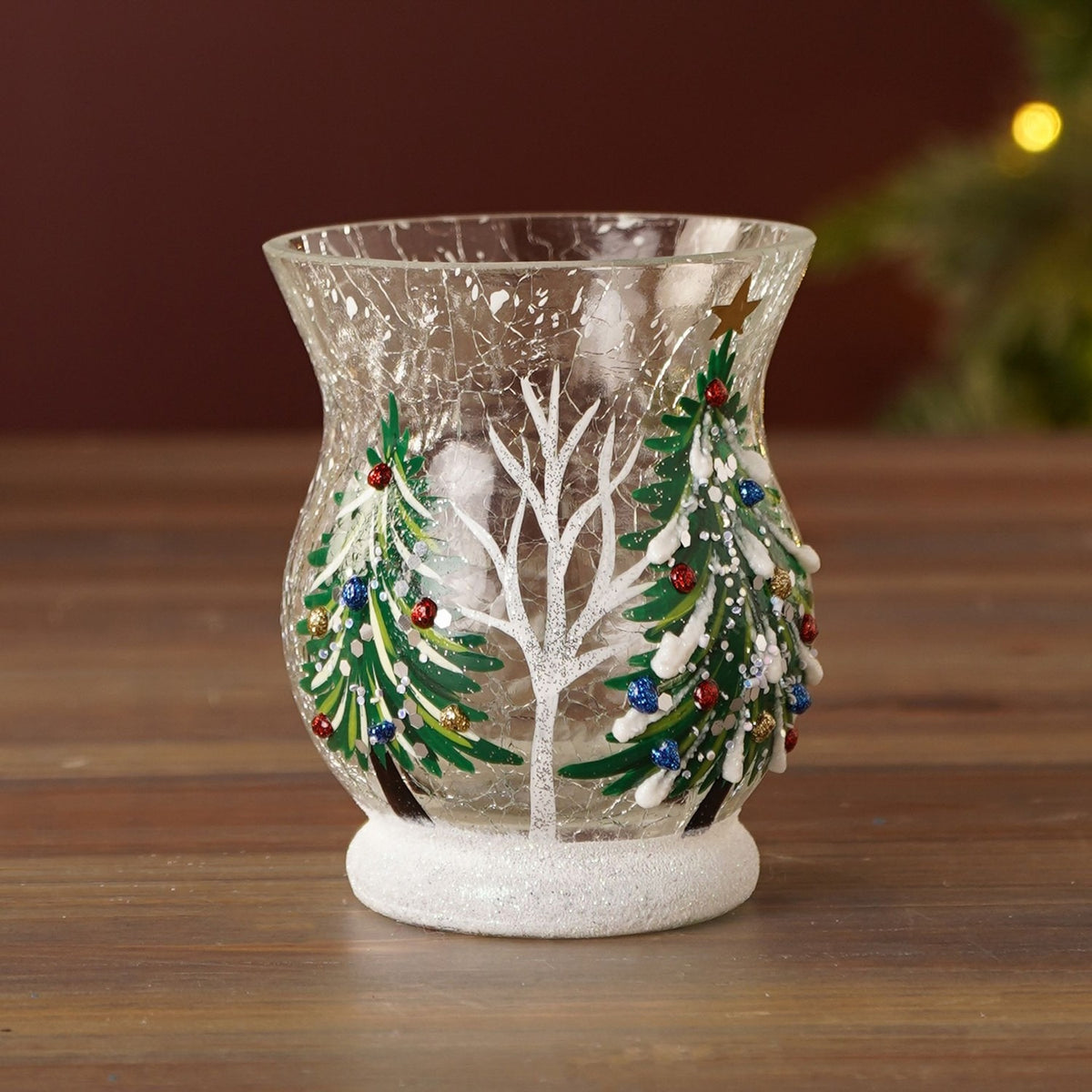Crackle glass candle holder, 9.5cm, with hand-painted green pine trees and a bare white tree, red, blue and gold baubles, gold star, and a white glitter base.