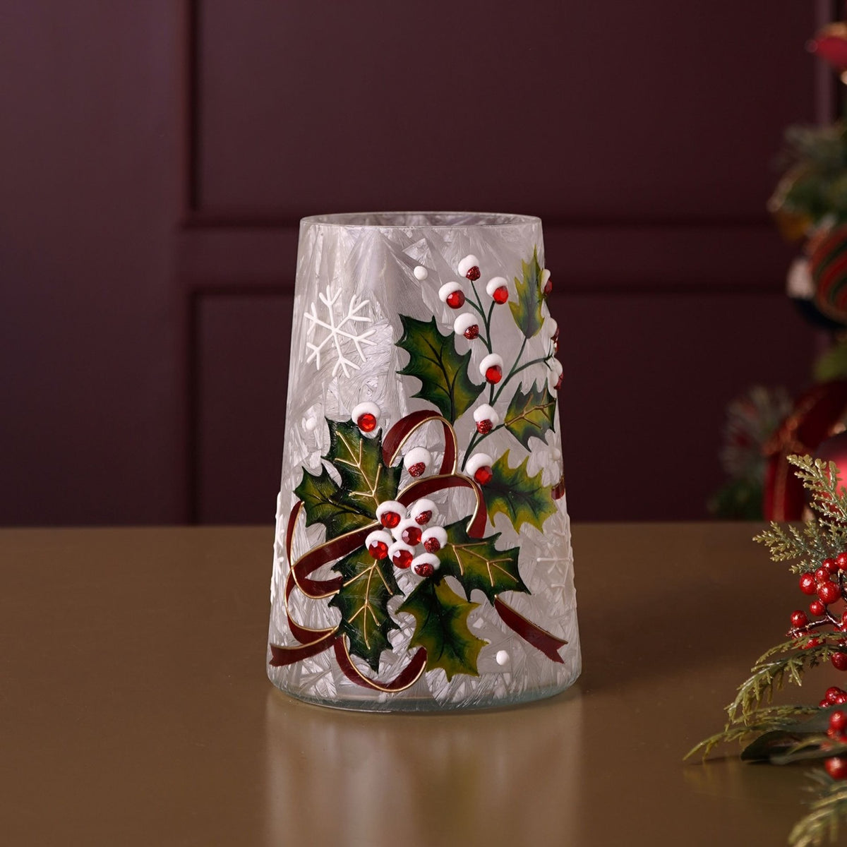 Tapered crackle glass vase, 18.2cm, with hand-painted holly leaves, red berries, white snowflake accents and a ribbon detail, shown on a wooden surface against a dark red wall.