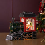 LED Glitter Santa Train Light-Up Decoration, 21.5cm, with a green boiler, red cab under an antiqued silver roof, and Santa visible inside beside a tree, shown on a table near a Christmas tree.