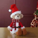 Sitting bear Christmas decoration in a red Santa suit with white fur trim, black belt, and red, black and white striped scarf, seated against a dark red background.