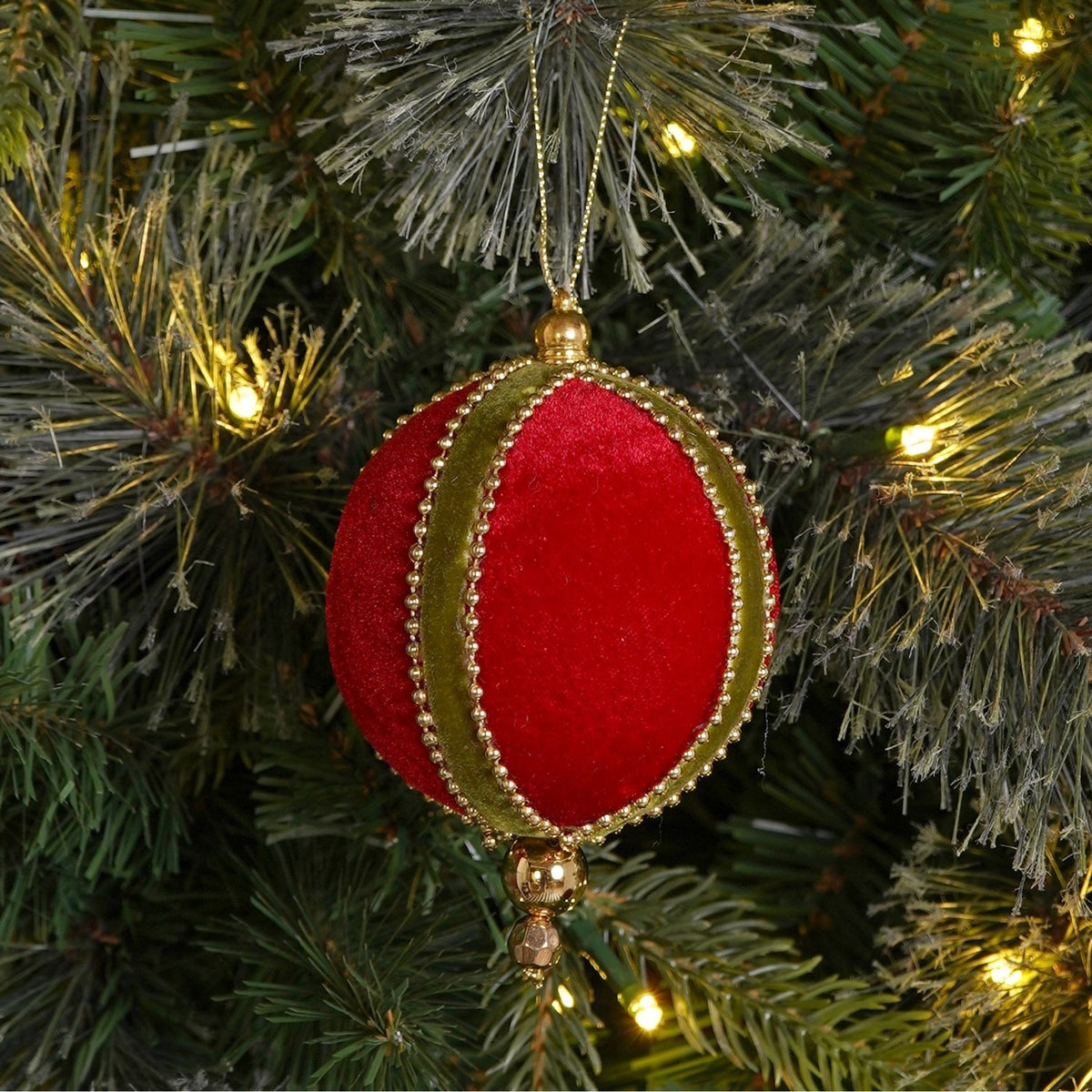 Round hanging bauble Christmas tree decoration in red velvet with green bands, edged in gold-coloured beads and gold bead accents, shown hanging on a pine tree.