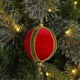 Round hanging bauble Christmas tree decoration in red velvet with green bands, edged in gold-coloured beads and gold bead accents, shown hanging on a pine tree.