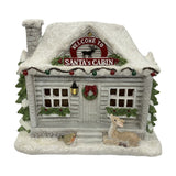 Snowy Santa Cabin Light-Up Decoration, 21cm, log cabin with glittering roof, stone chimney, fir trees, wreath, lit window and porch light, deer and bird figures.