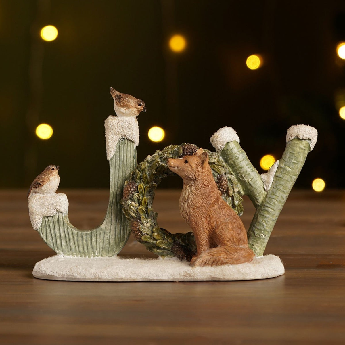 Joy Resin Mantel Plaque with Fox, sage green JOY letters with snowy tops, two birds perched on the J, a pine-cone wreath forming the O, and a sitting russet fox, on a snow-dusted base.