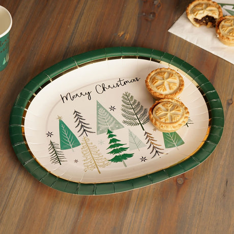 Oval Christmas paper plate in cream with a dark green rim, printed with "Merry Christmas" script and green, sage and gold tree designs, shown on a wooden table with mince pies.