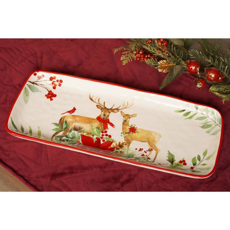 Rectangular white ceramic serving plate with red rim, 35cm, featuring a painted stag and doe scene with holly, berries and poinsettia, shown on a red fabric surface with festive greenery.