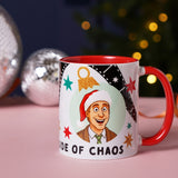 Stoneware mug with red interior and handle, featuring a cartoon man in a Santa hat, film strips, stars, gold ornament, and Side of Chaos text, shown beside disco balls and Christmas lights.