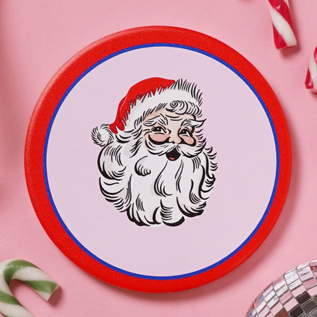 Round ceramic coaster with a vintage-style Santa's head design in white and red, featuring a curling beard and red hat, bordered by a thin blue ring and bold red edge.