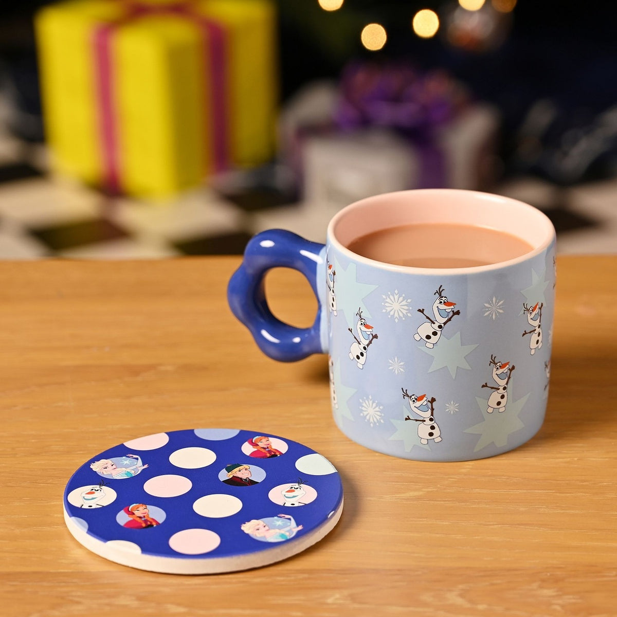 Frozen Snowman porcelain mug, 250ml, blue with Olaf print and pink interior, scalloped blue handle, shown with matching round polka-dot coaster on a wooden table.